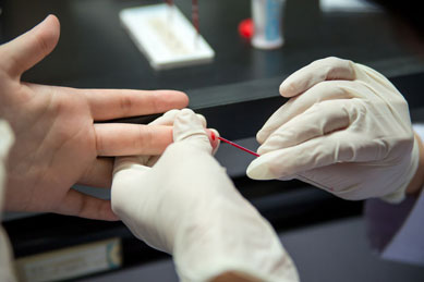 A medical professional drawing blood from patient's fingertip